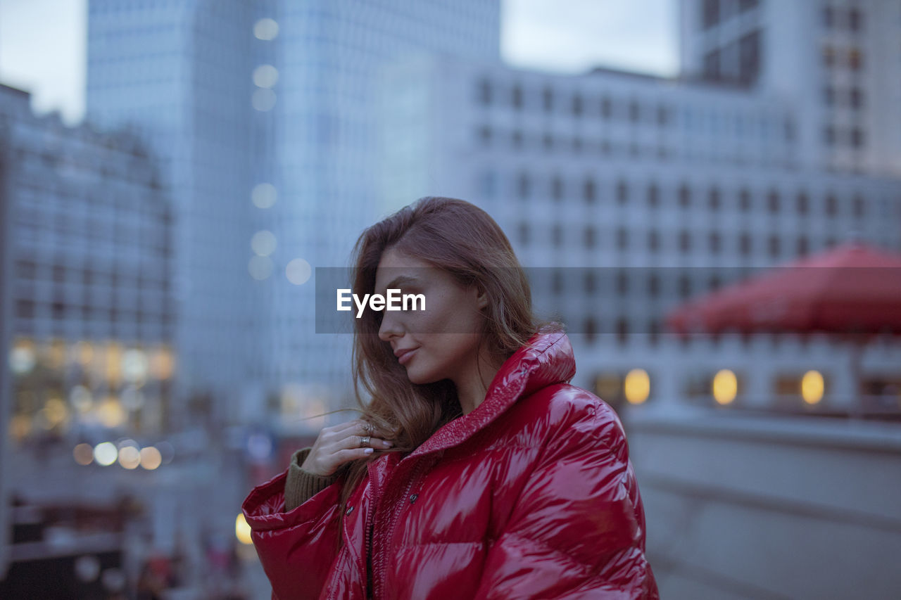 Close-up of thoughtful young woman wearing warm clothing in city during sunset