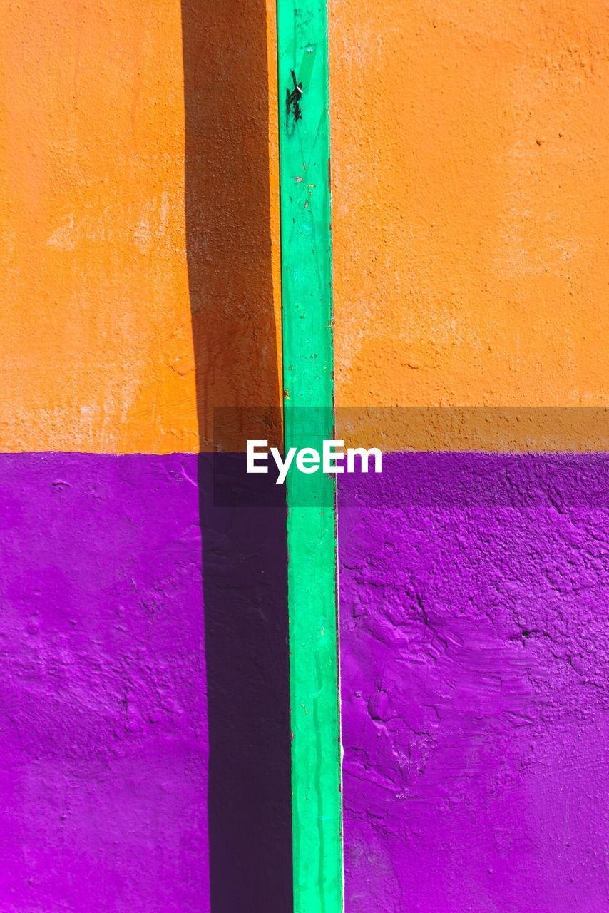 Green rod against orange and purple wall