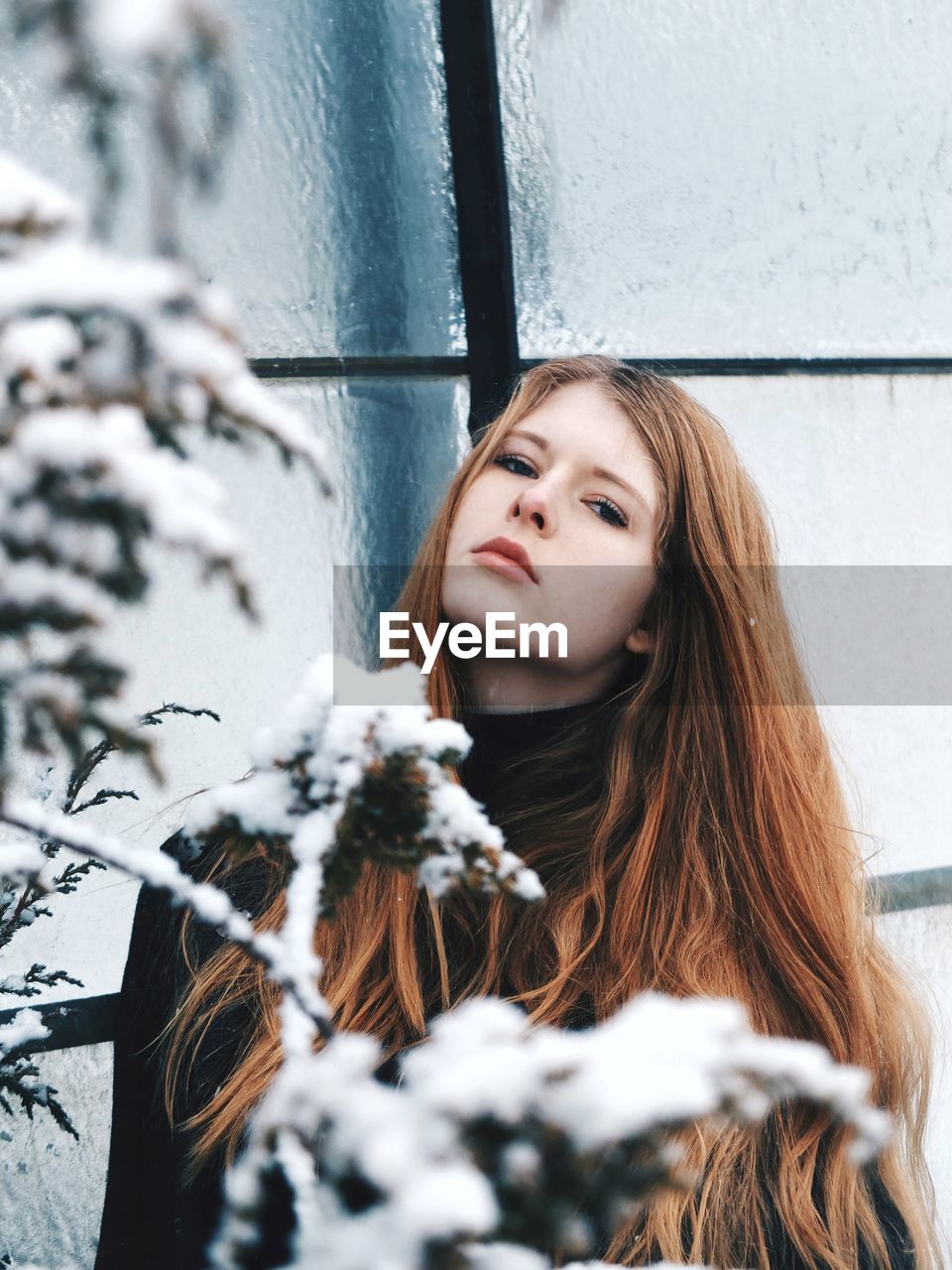 Portrait of young woman standing against window during winter