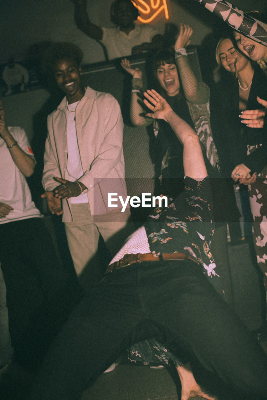 Young men and women cheering friend dancing while bending backwards at nightclub