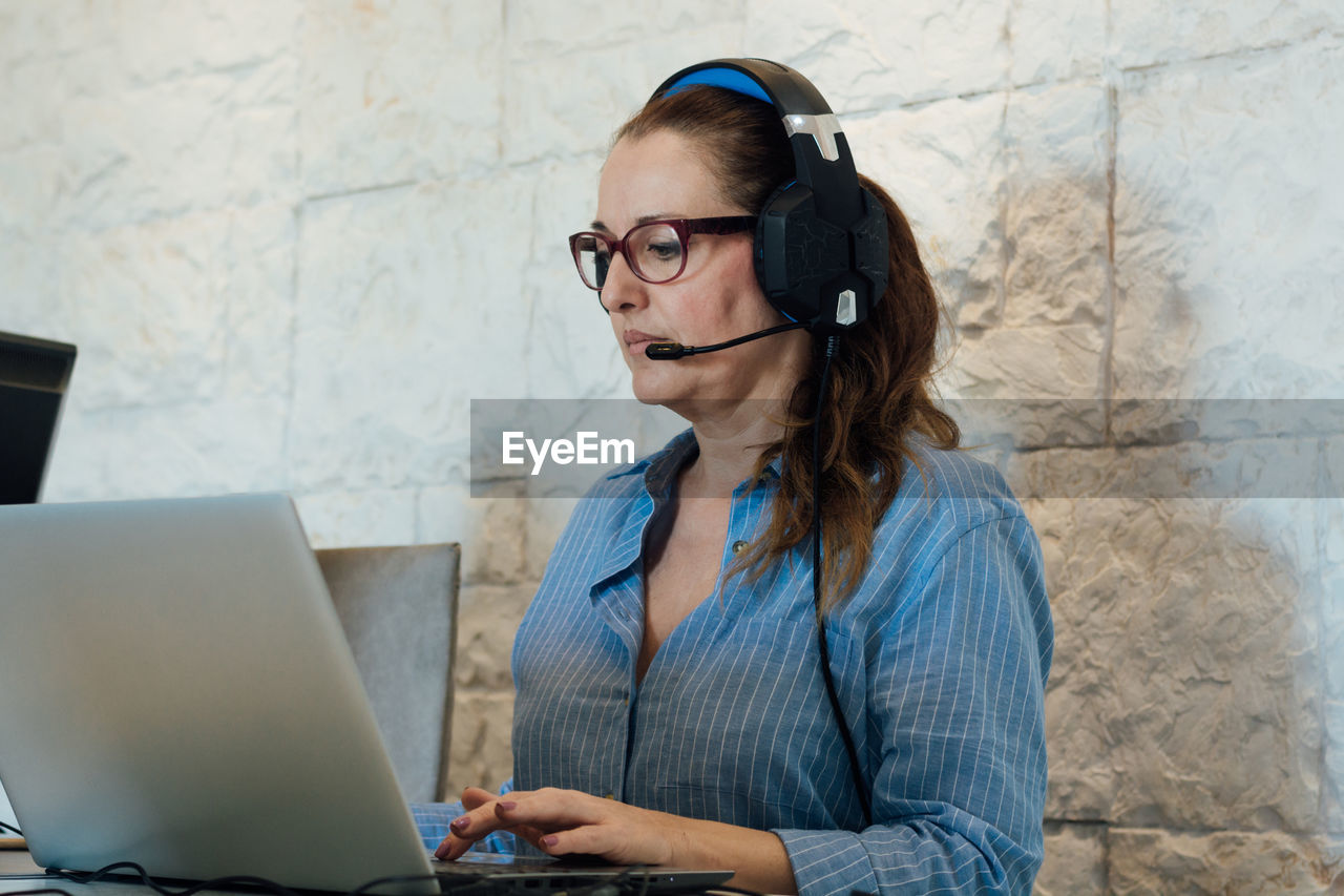 Woman working with her laptop and is focused on listening with her headphones