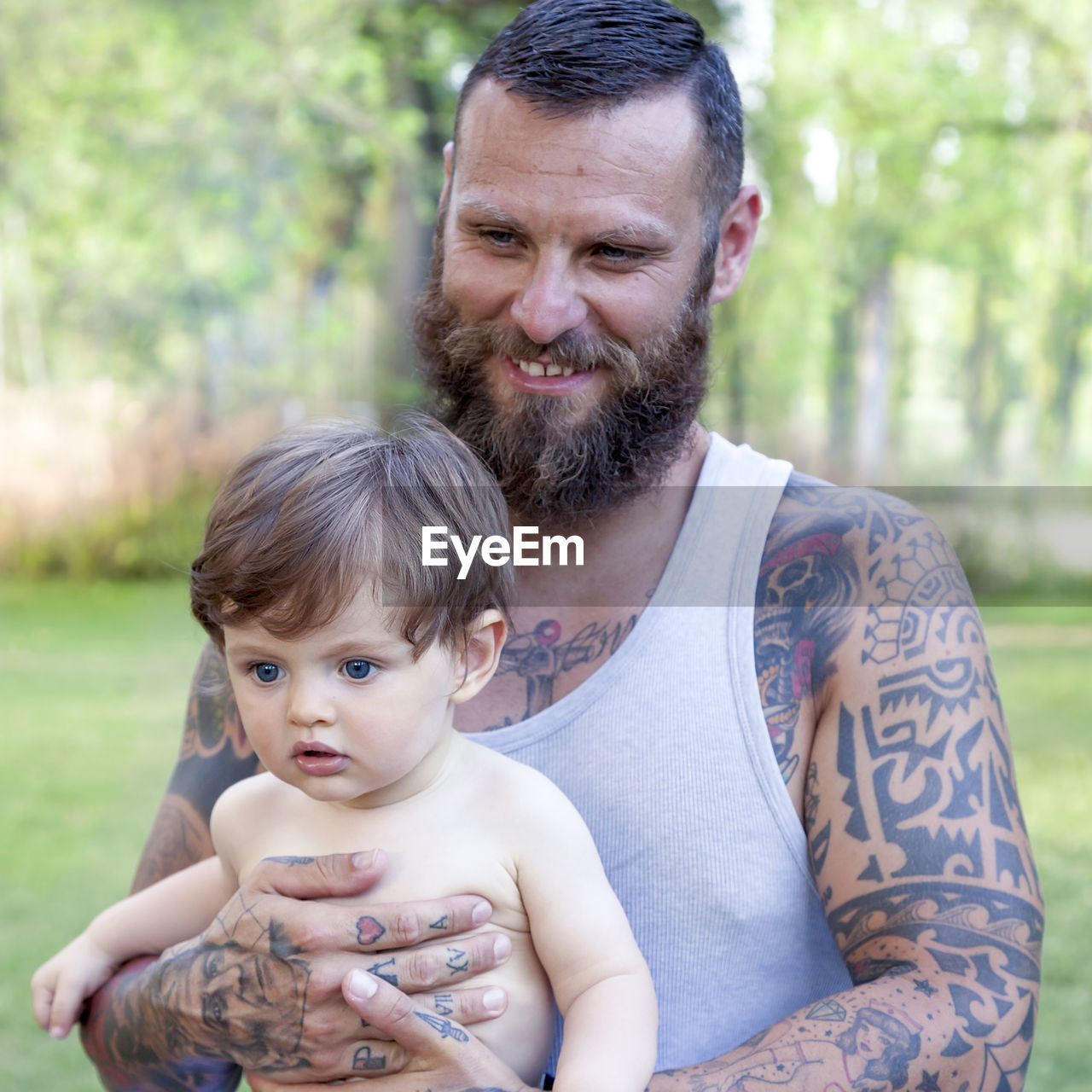 Smiling bearded man holding son standing in park 