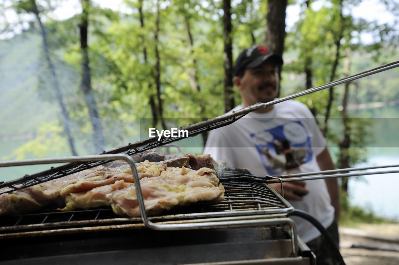 Close-up of meat cooking on barbecue grill with man standing in background