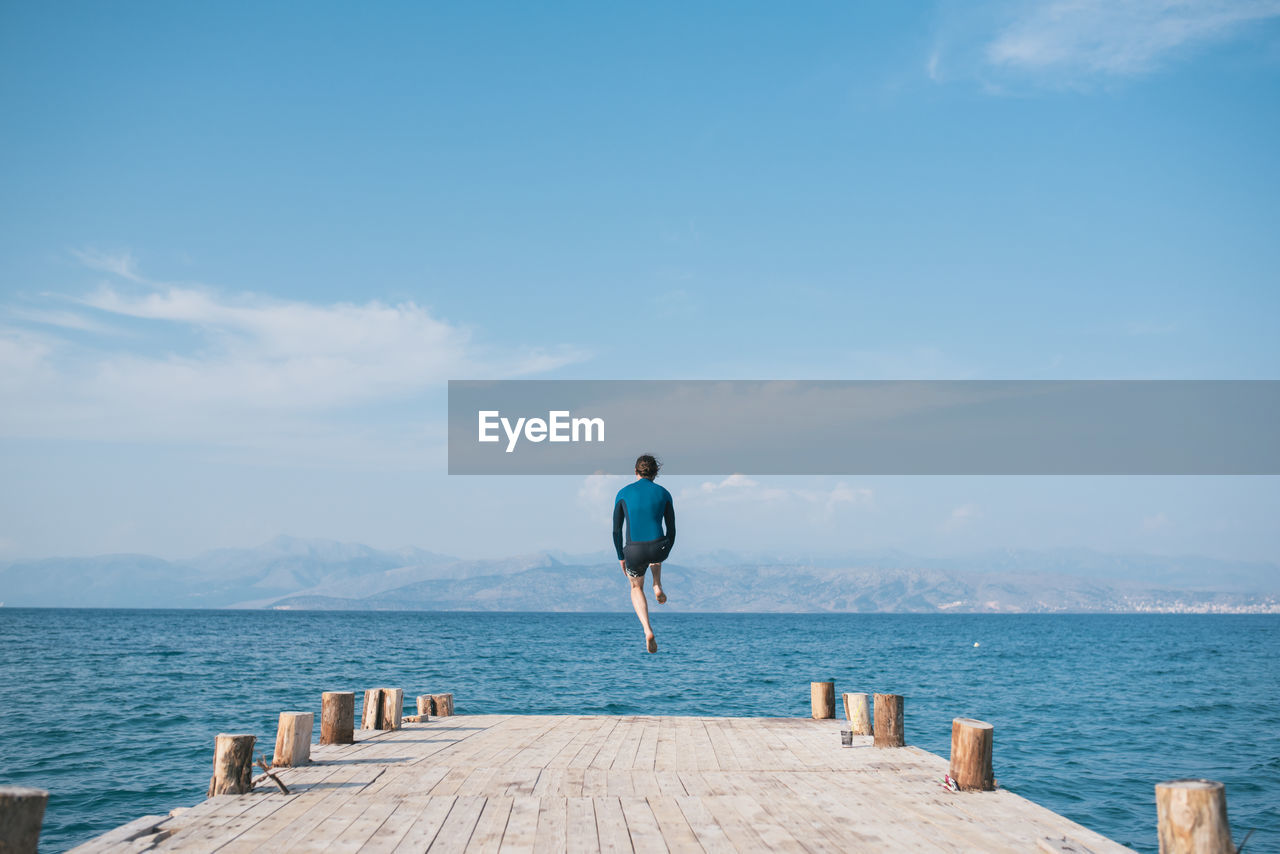 REAR VIEW OF MAN LOOKING AT SEA