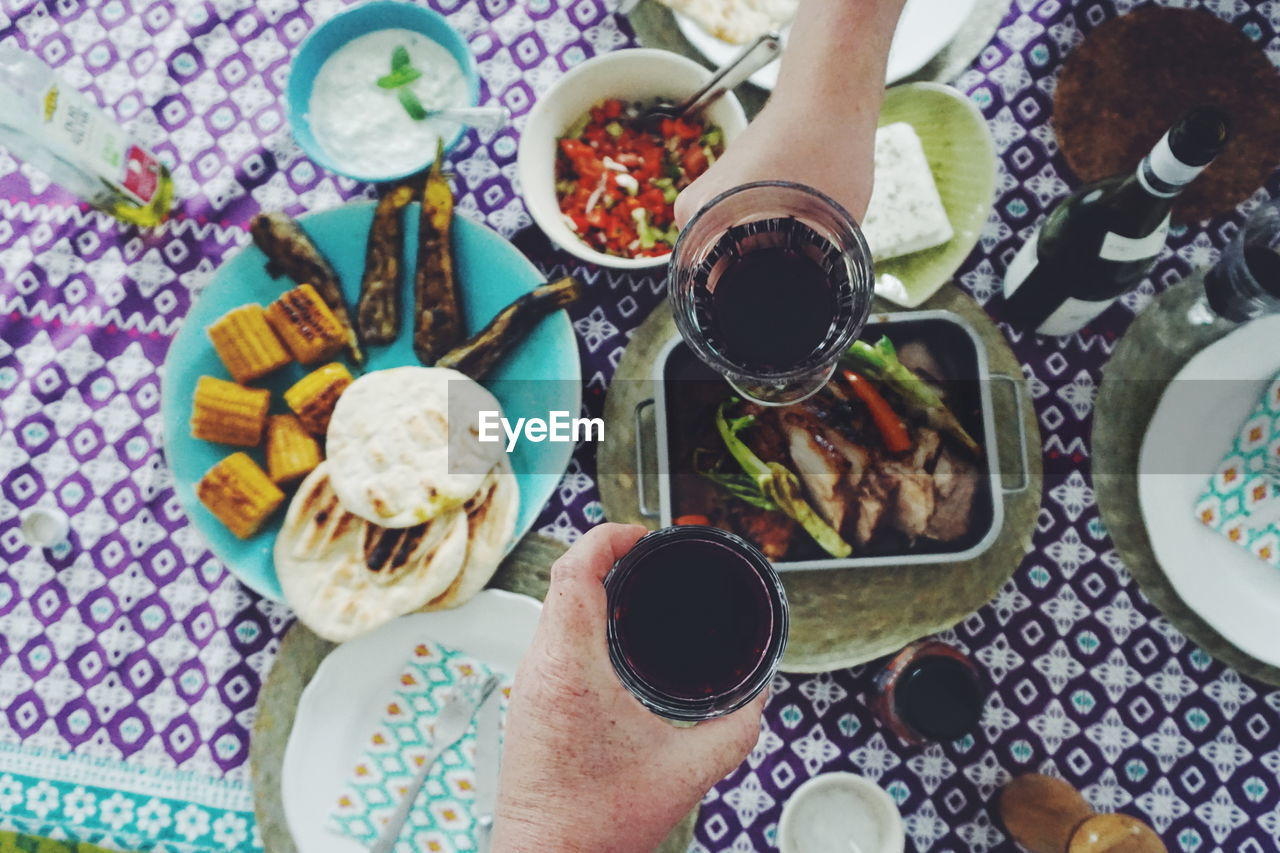 Cropped hands toasting drinks over food on table