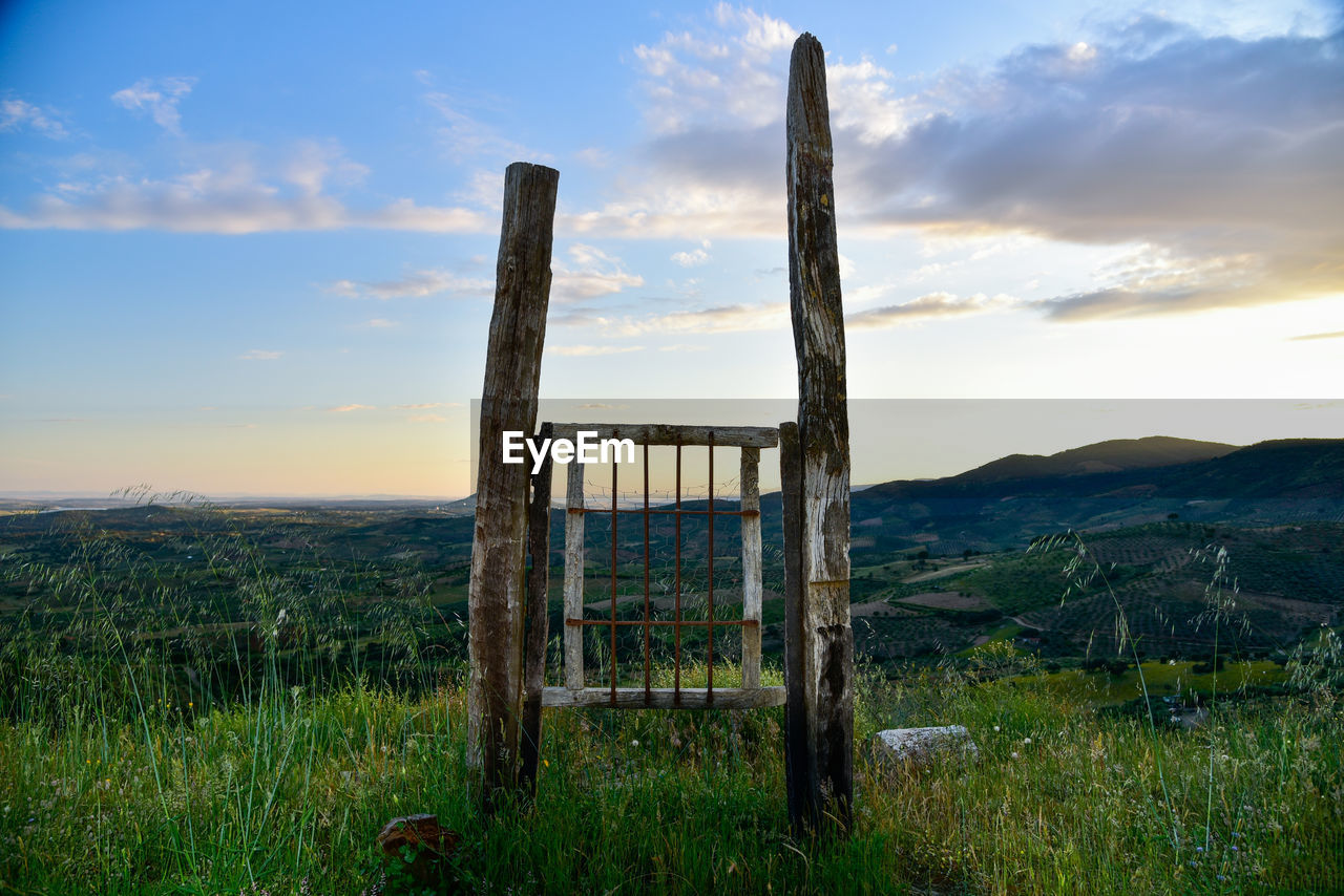 WOODEN POST ON FIELD AGAINST SKY