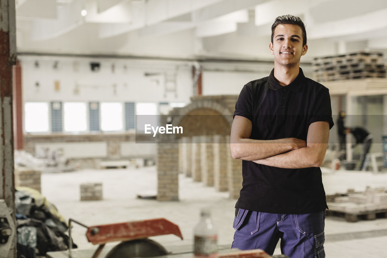 Portrait of confident carpentry student standing arms crossed at workshop