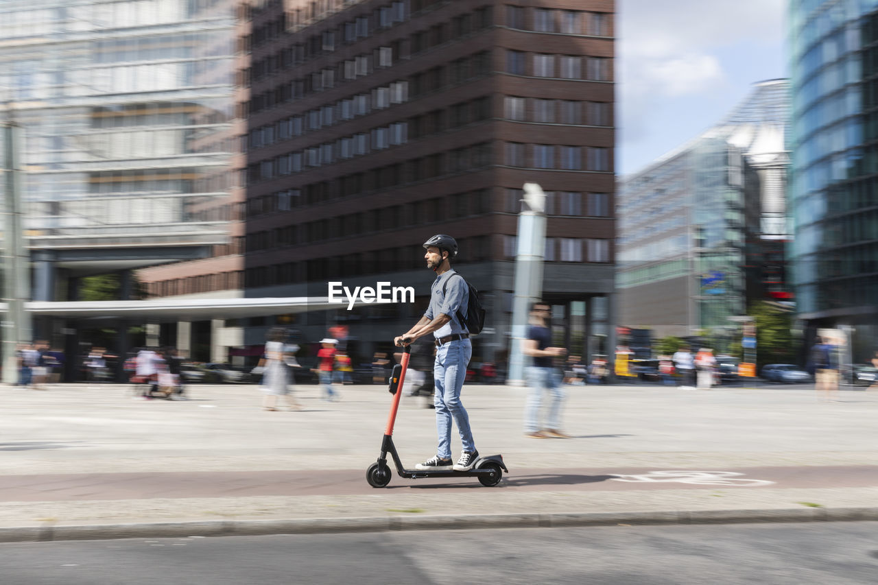 Businessman riding e-scooter on the pavement in the city, berlin, germany