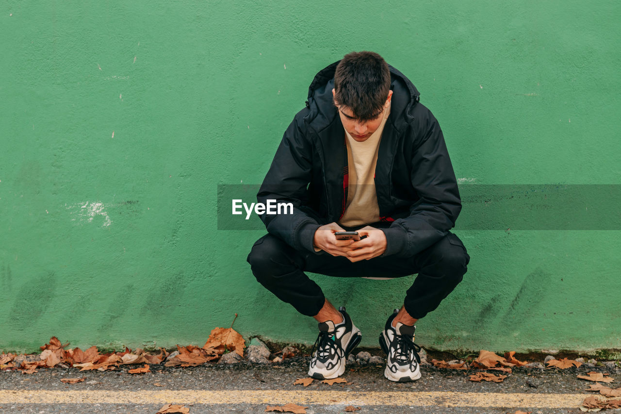 Full length of man sitting against wall