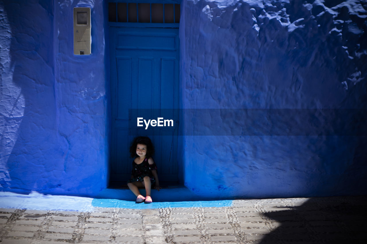 FULL LENGTH PORTRAIT OF WOMAN AGAINST BLUE WALL