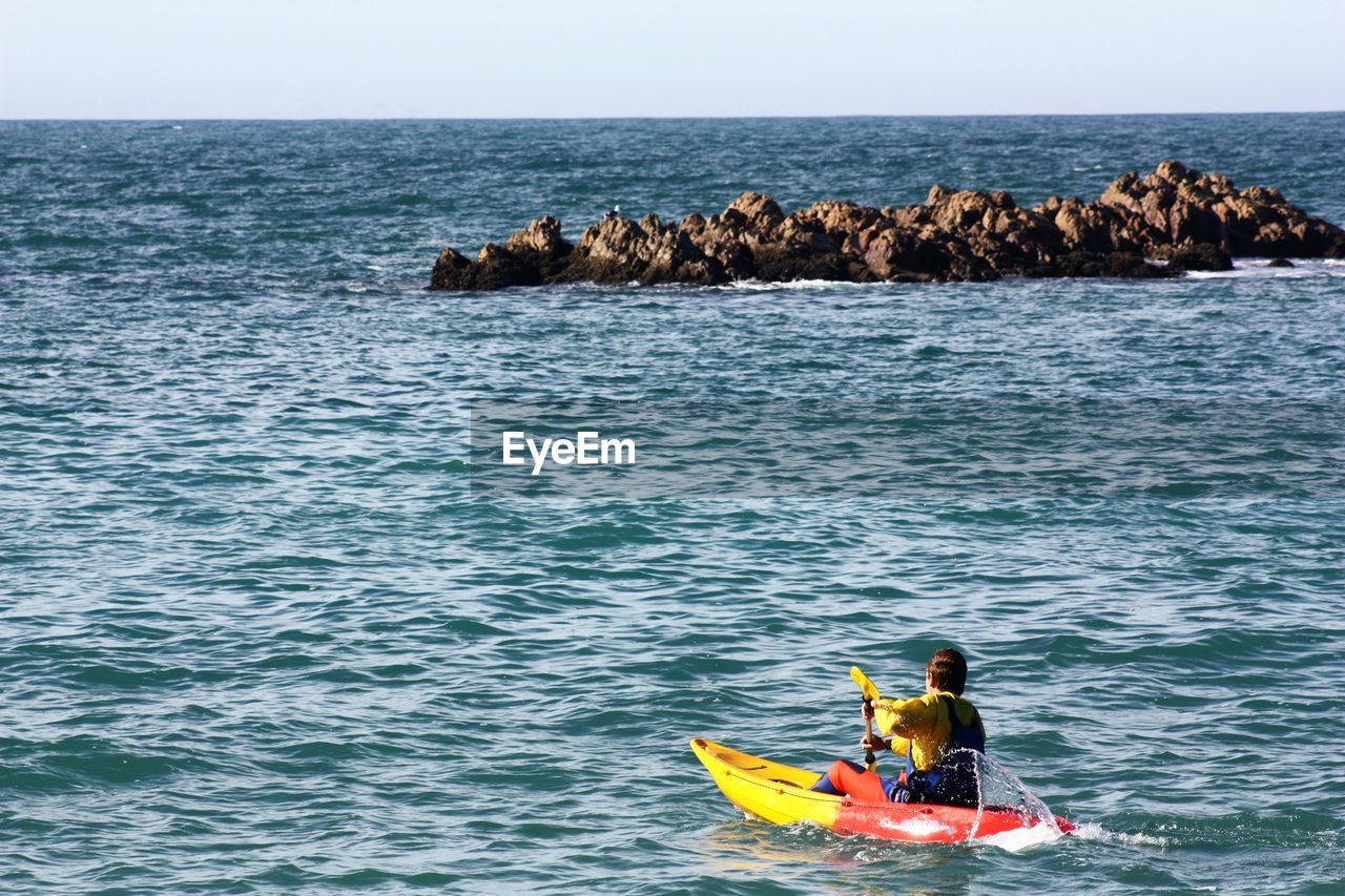 Rear view of man kayaking on sea against clear sky