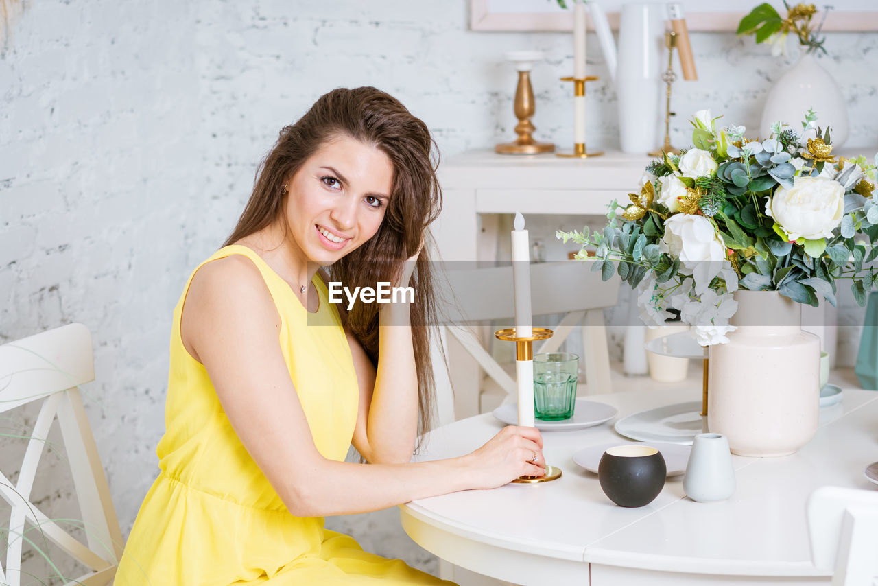 Happy woman sits at table in yellow dress smiling. there is beautiful bouquet