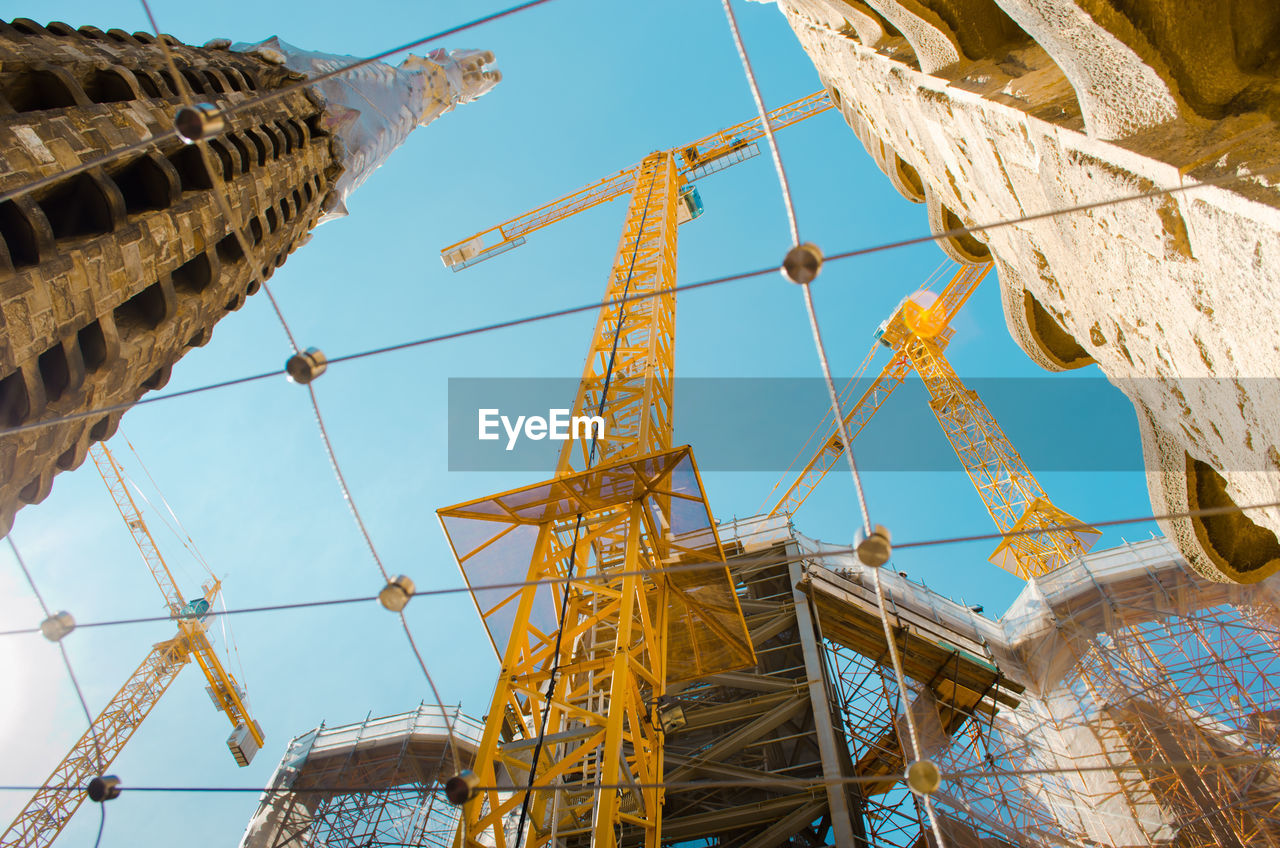 Low angle view of yellow metallic cranes at sagrada familia against sky