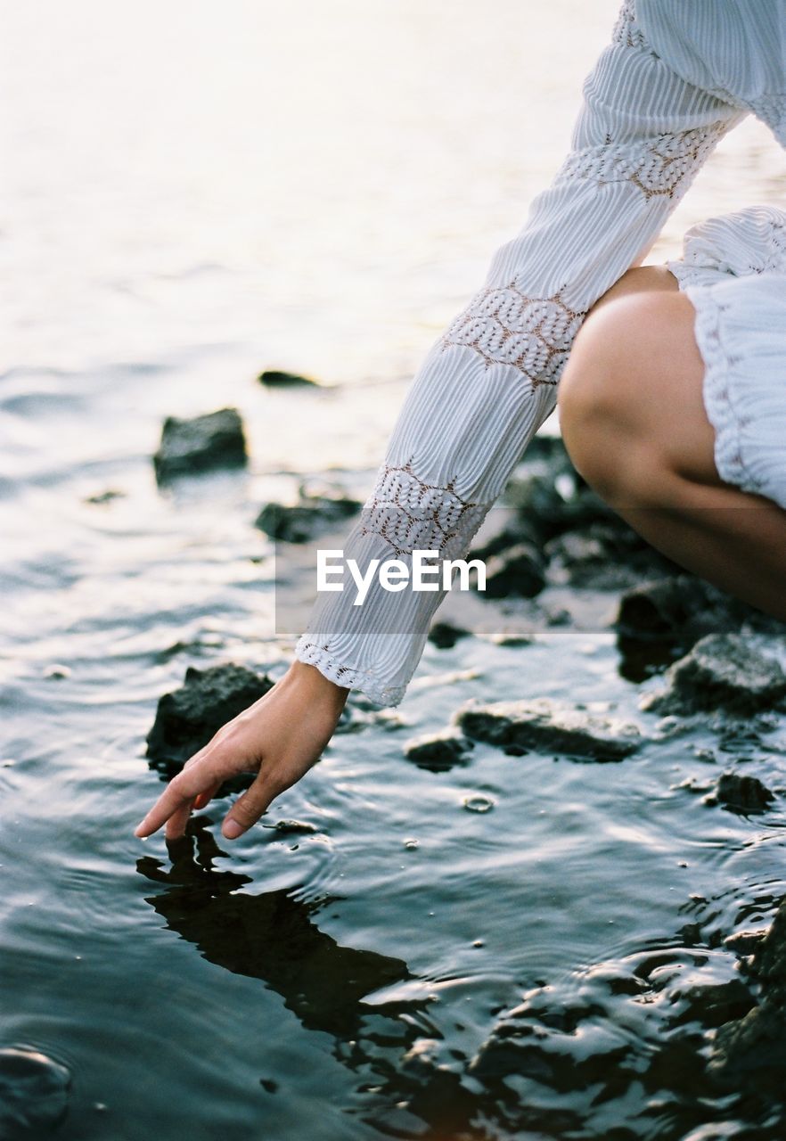 Midsection of woman touching water in sea