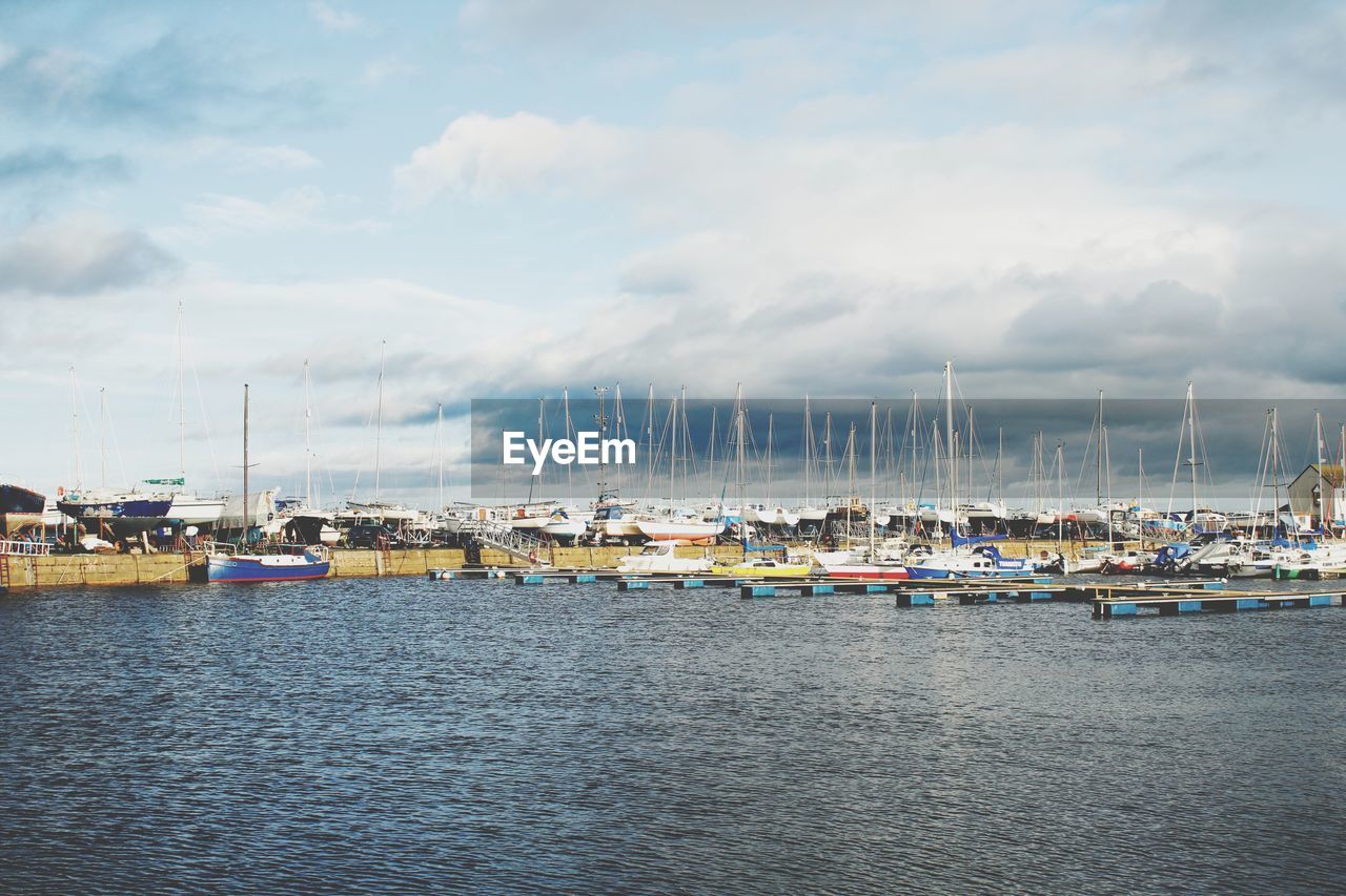 Sailboats moored at harbor against sky