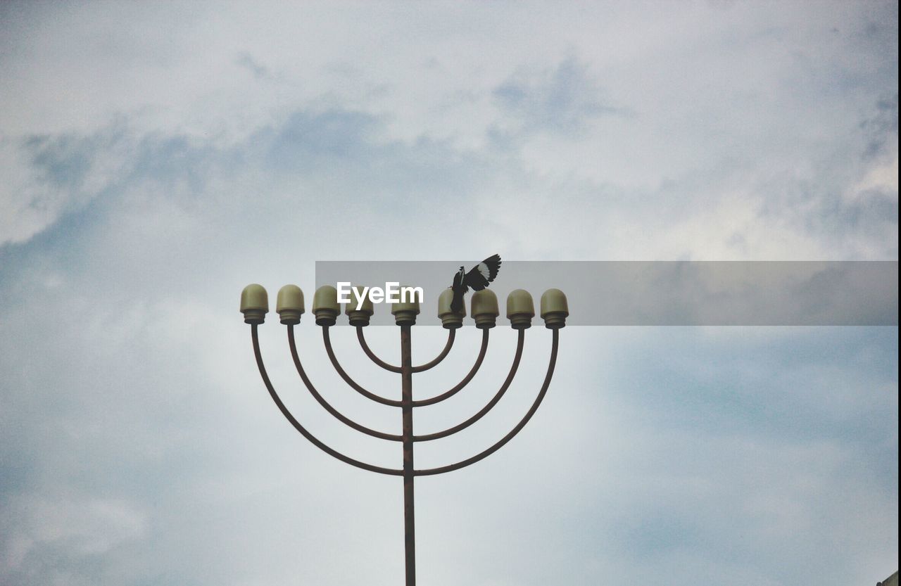 Bird sitting on street light against cloudy sky