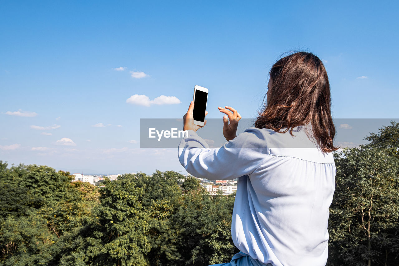 Rear view of woman photographing against sky