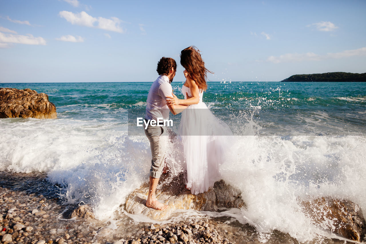 Young couple standing at beach against sky