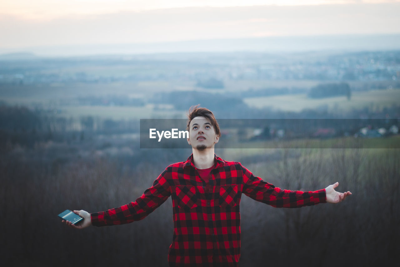 Candid portrait of a man in his 20s dressed in a black and red checked shirt joyfully facing the sky