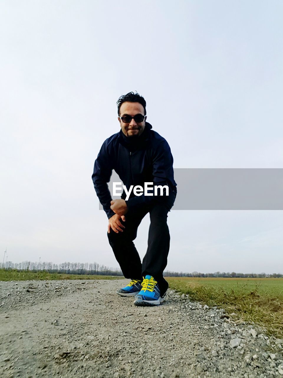 Portrait of young man bending on field against clear sky