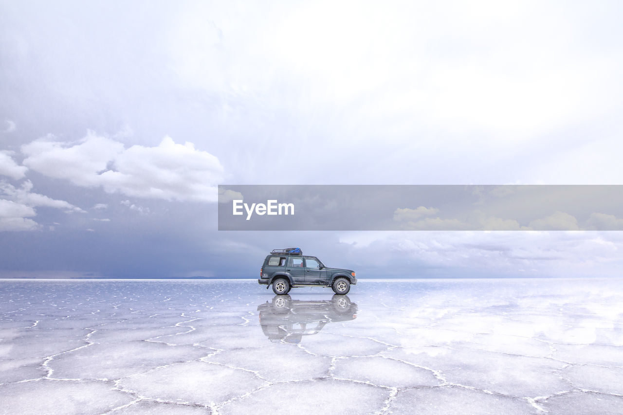 Side view of car on frozen lake against sky