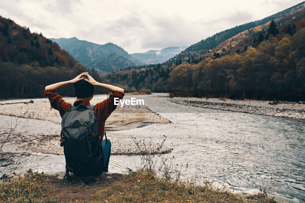 REAR VIEW OF MAN ON SHORE AGAINST MOUNTAINS