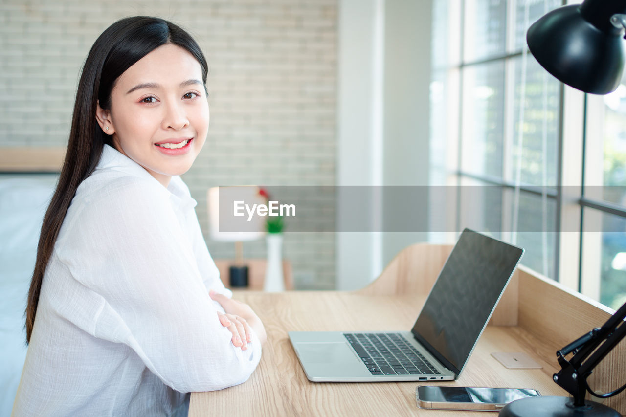 Portrait of smiling young woman using laptop on table