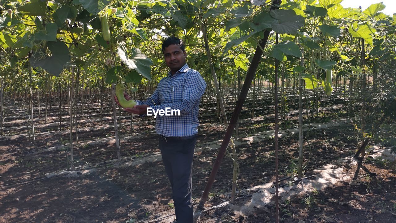 Portrait of man holding calabash while standing on field