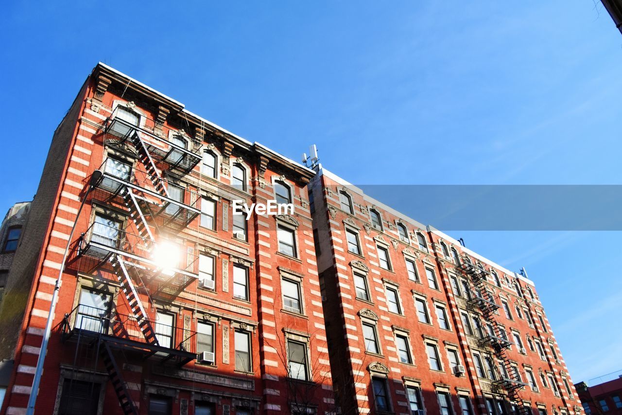 Low angle view of building against blue sky - traditional townhouse with fire escape in east village