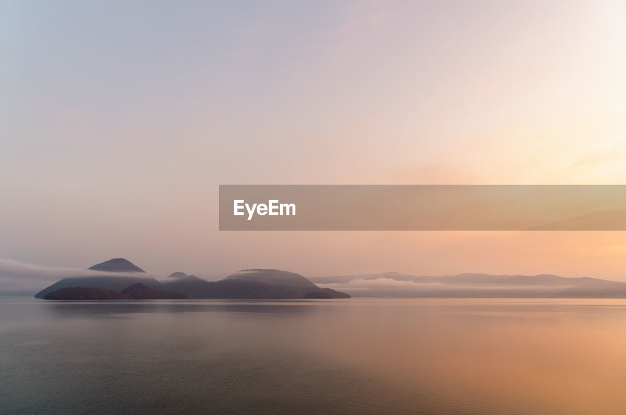 Distant island in foggy lake surface under warm color sky in early morning