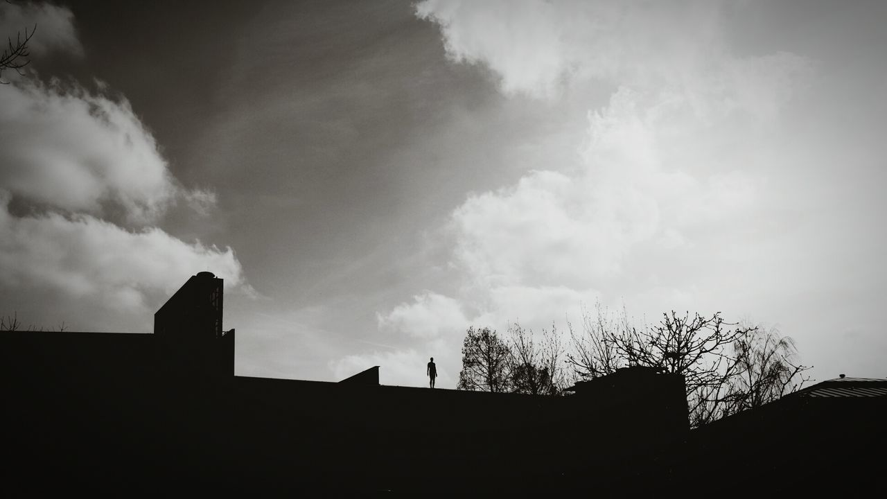 Low angle view of silhouette person standing on building against cloudy sky