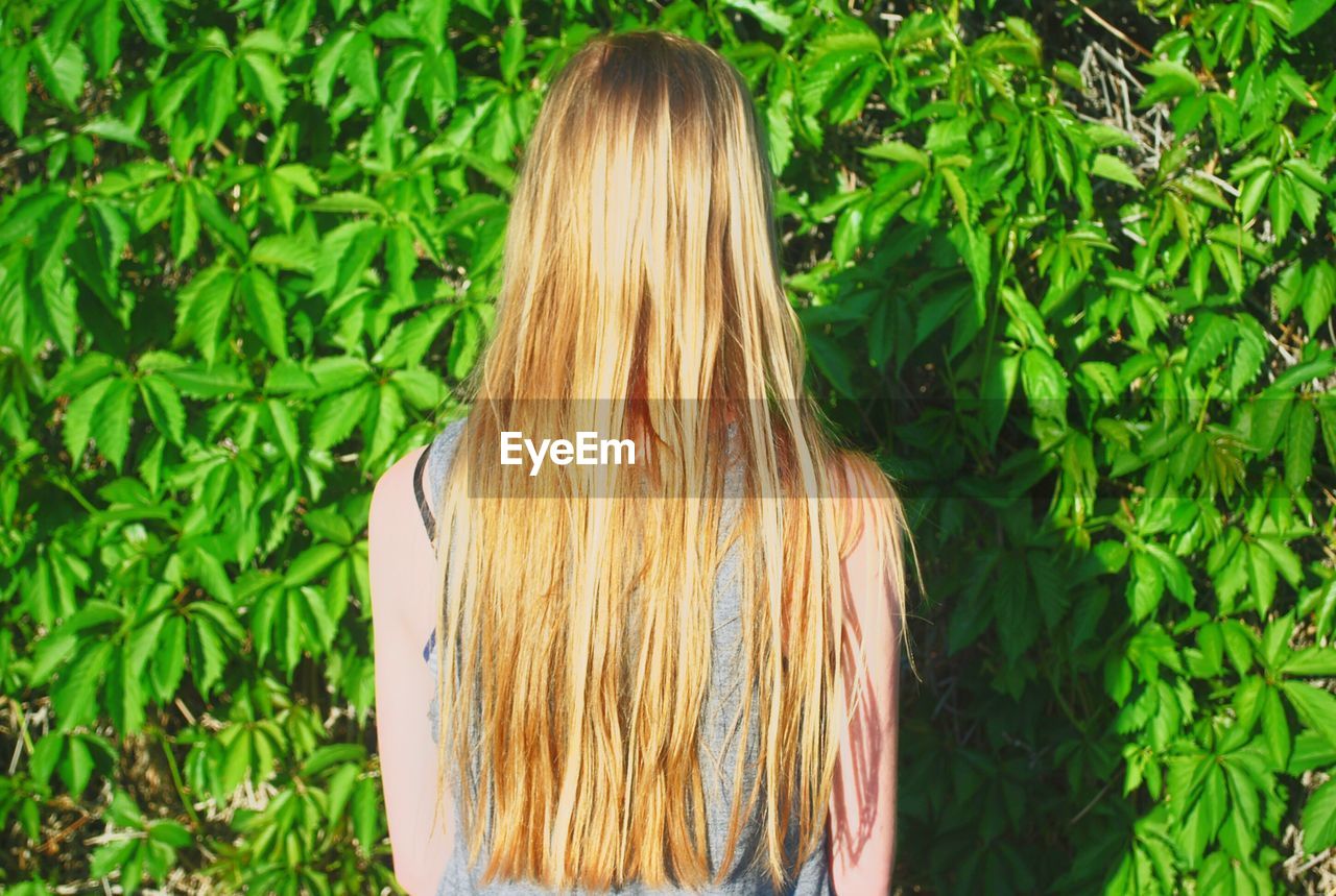 Rear view of woman with blond hair standing against plants