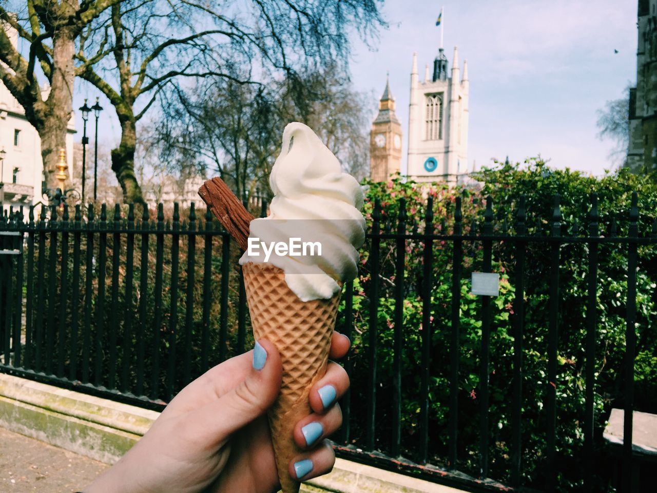 Cropped image of woman hand holding ice cream cone on footpath against big ben