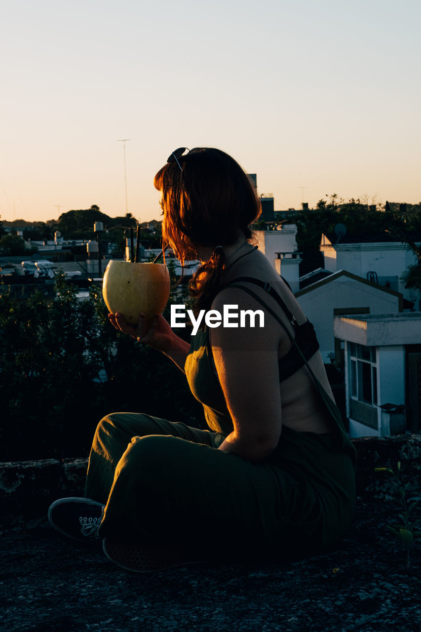 Woman drinking with a melon on the rooftop during sunset