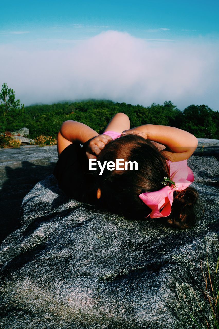 Girl lying on rock at beach against sky