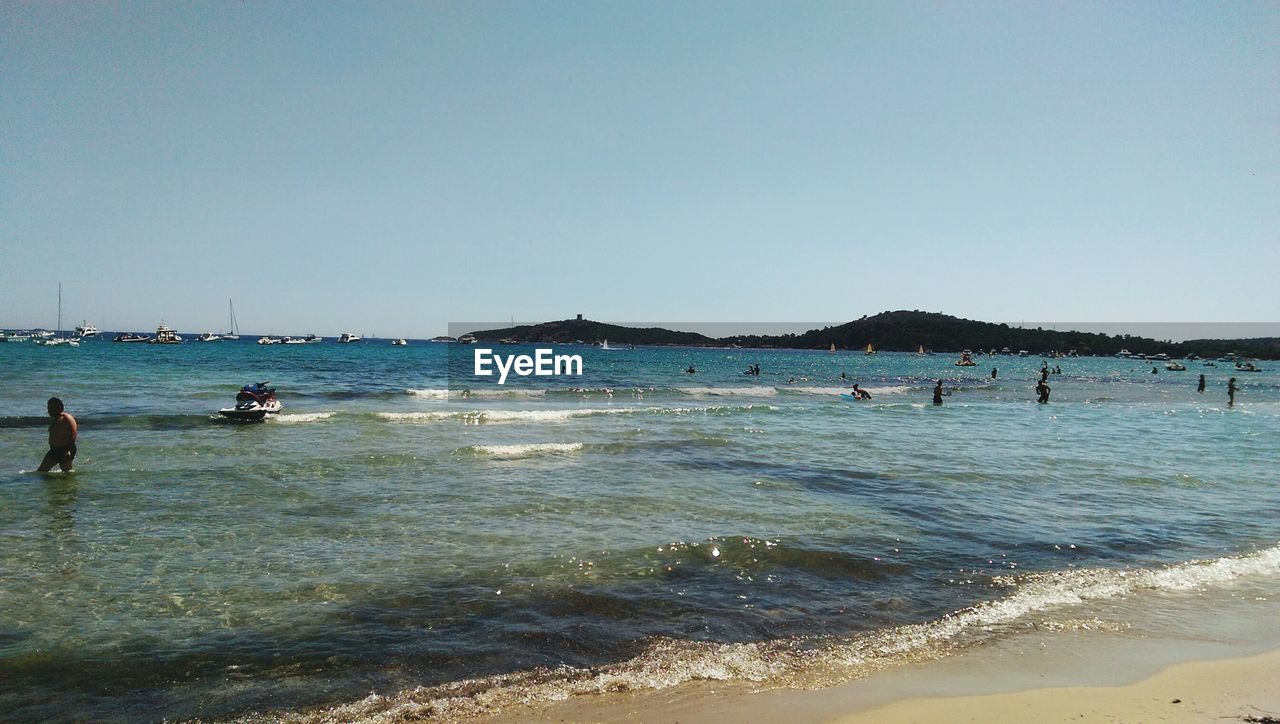 TOURISTS ON BEACH AGAINST CLEAR SKY