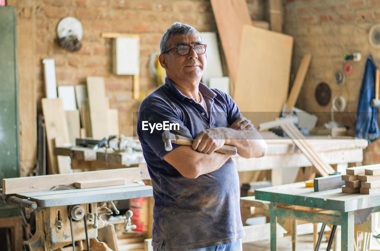 Elderly carpenter posing with crossed arms in his workshop