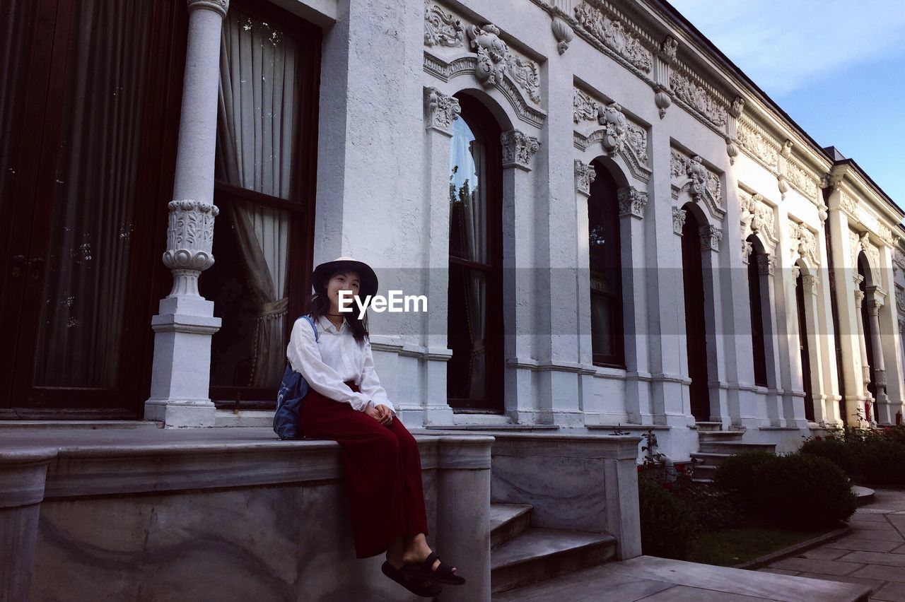 YOUNG WOMAN SITTING OUTSIDE BUILDING