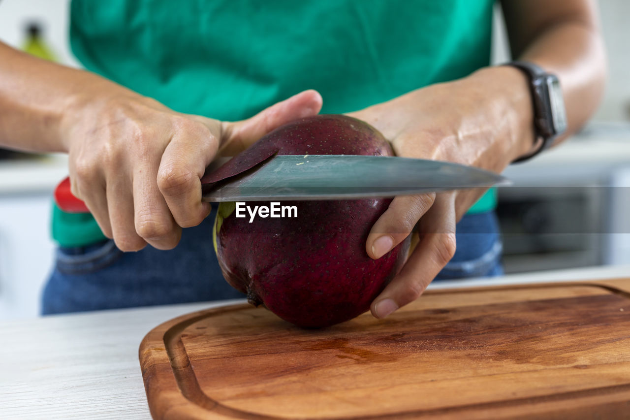 Woman cutting a mango in the kitchen on a wooden board