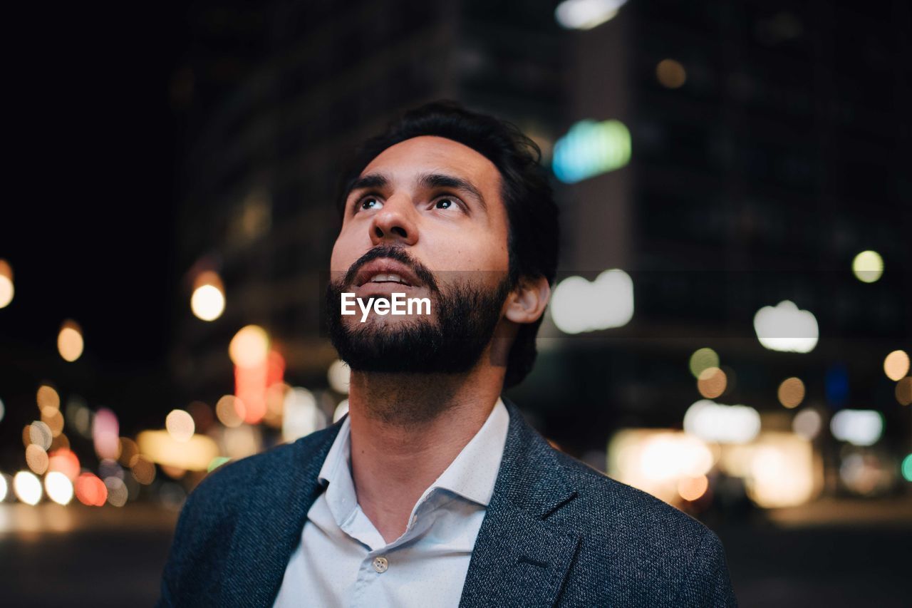 Contemplating man looking up while standing in city at night