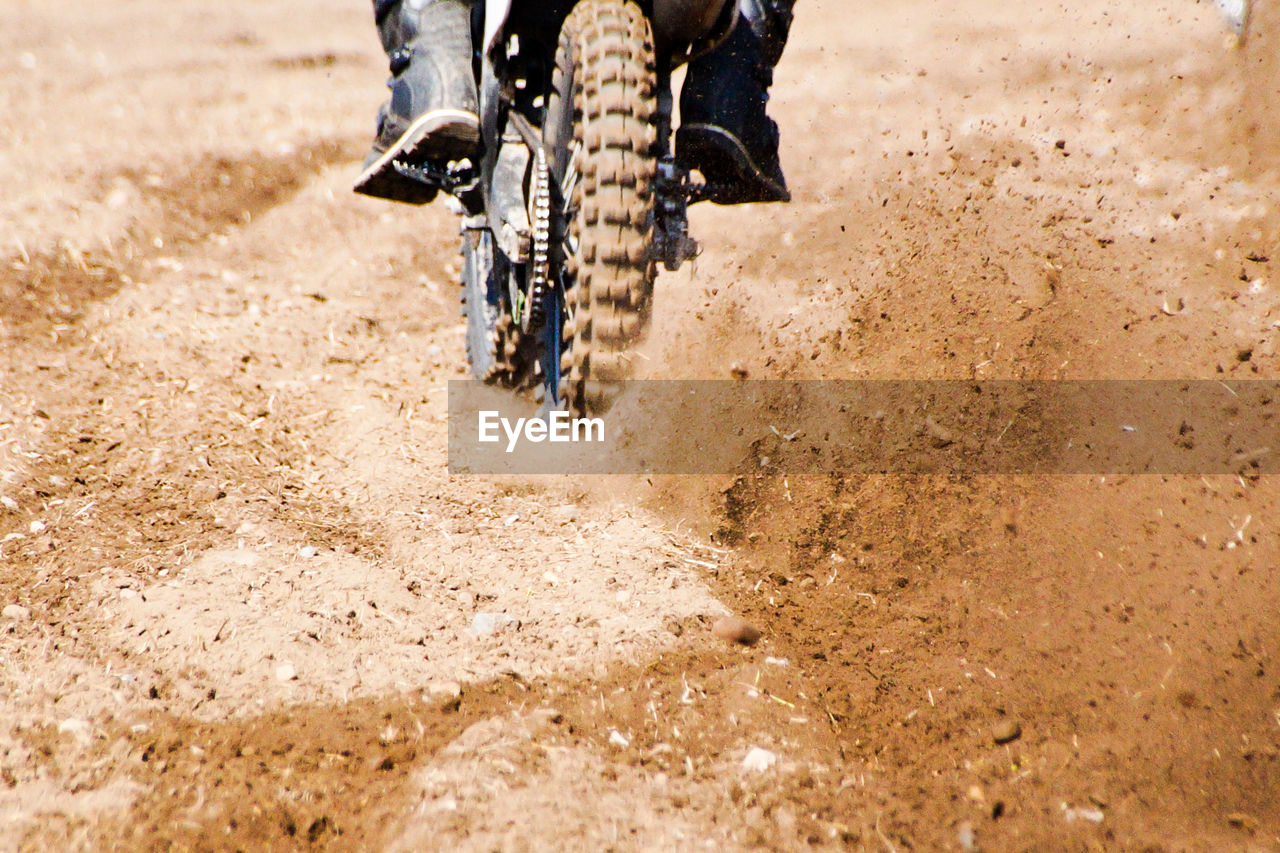 Low section of person riding motorcycle on dirt road