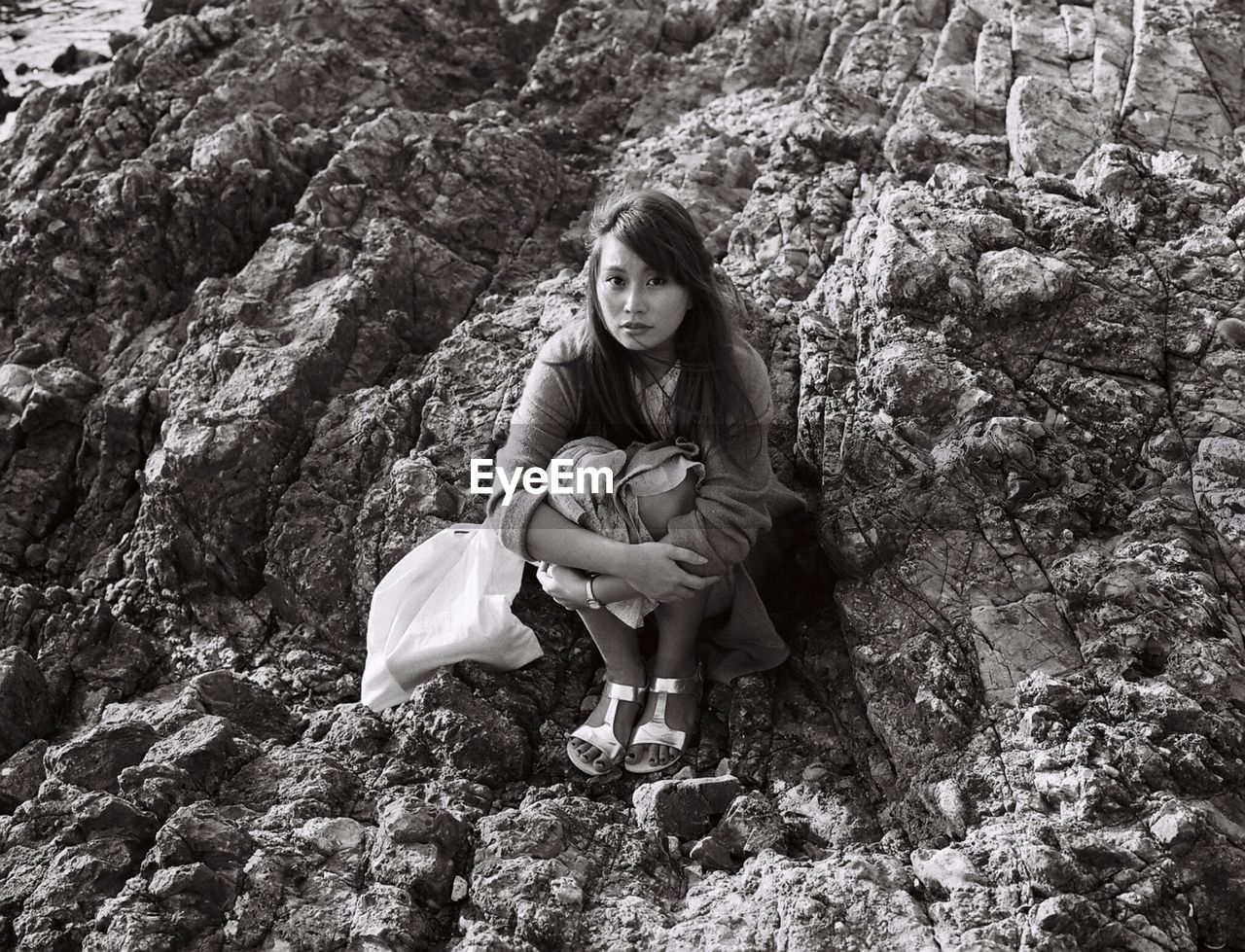 Full length portrait of woman sitting on rock