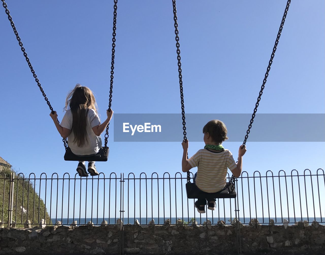 Rear view of children sitting on swing at playground