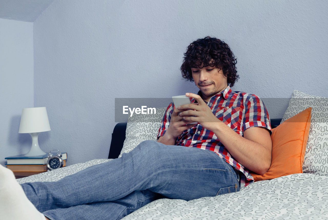 Close-up of man using mobile phone while sitting on bed at home