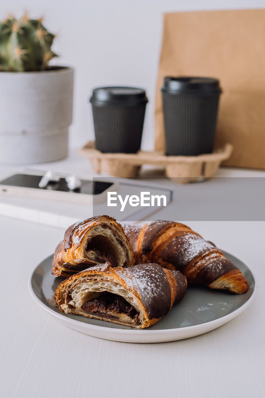 Close up of chocolate croissants with cups of coffee and notepad with smartphone on the background