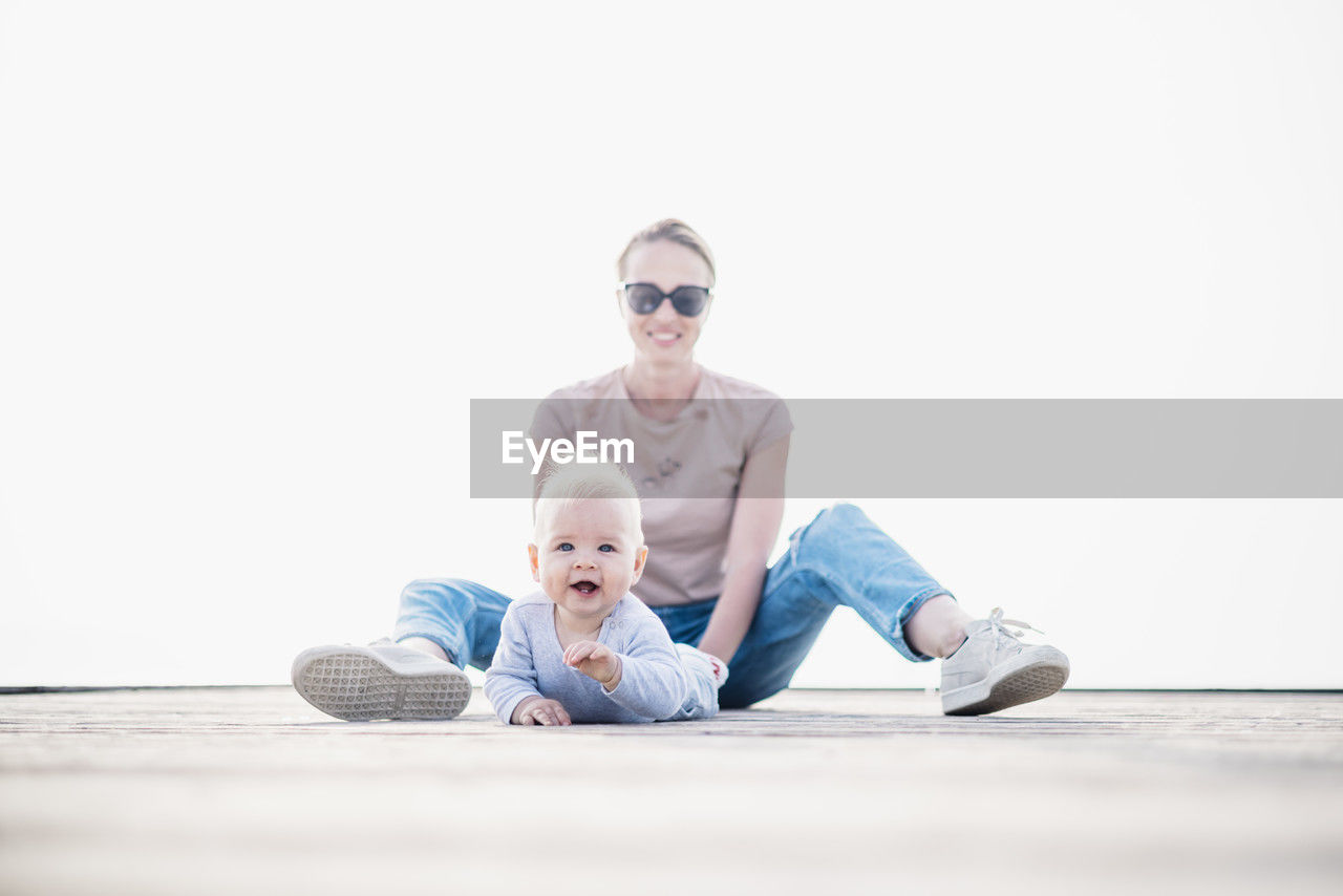 full length of woman sitting on wooden table against white background