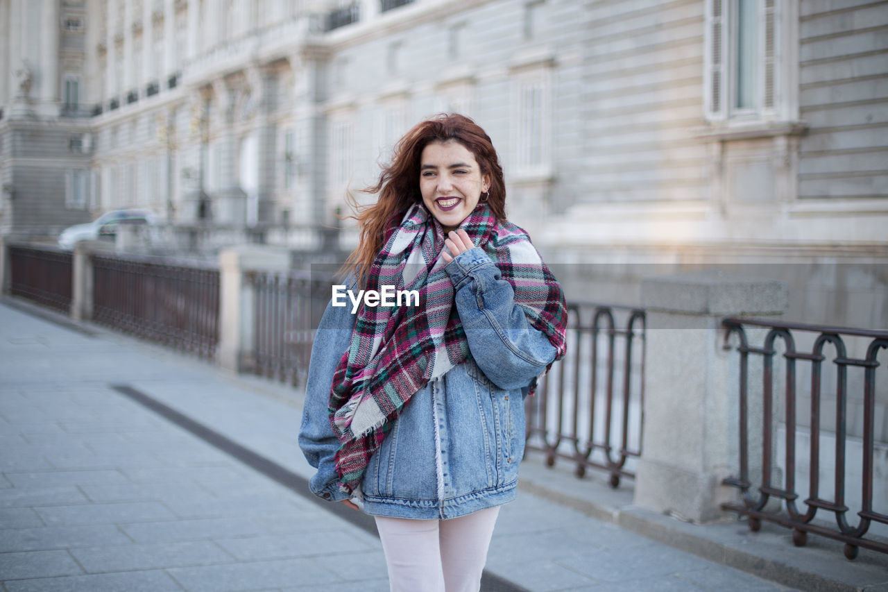 Smiling young woman looking away while standing against built structure