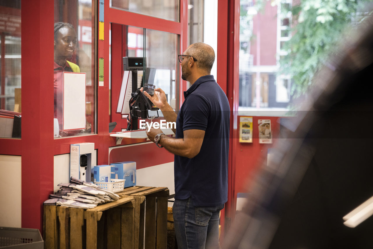 Mature man paying through mobile payment while standing at checkout counter in hardware store