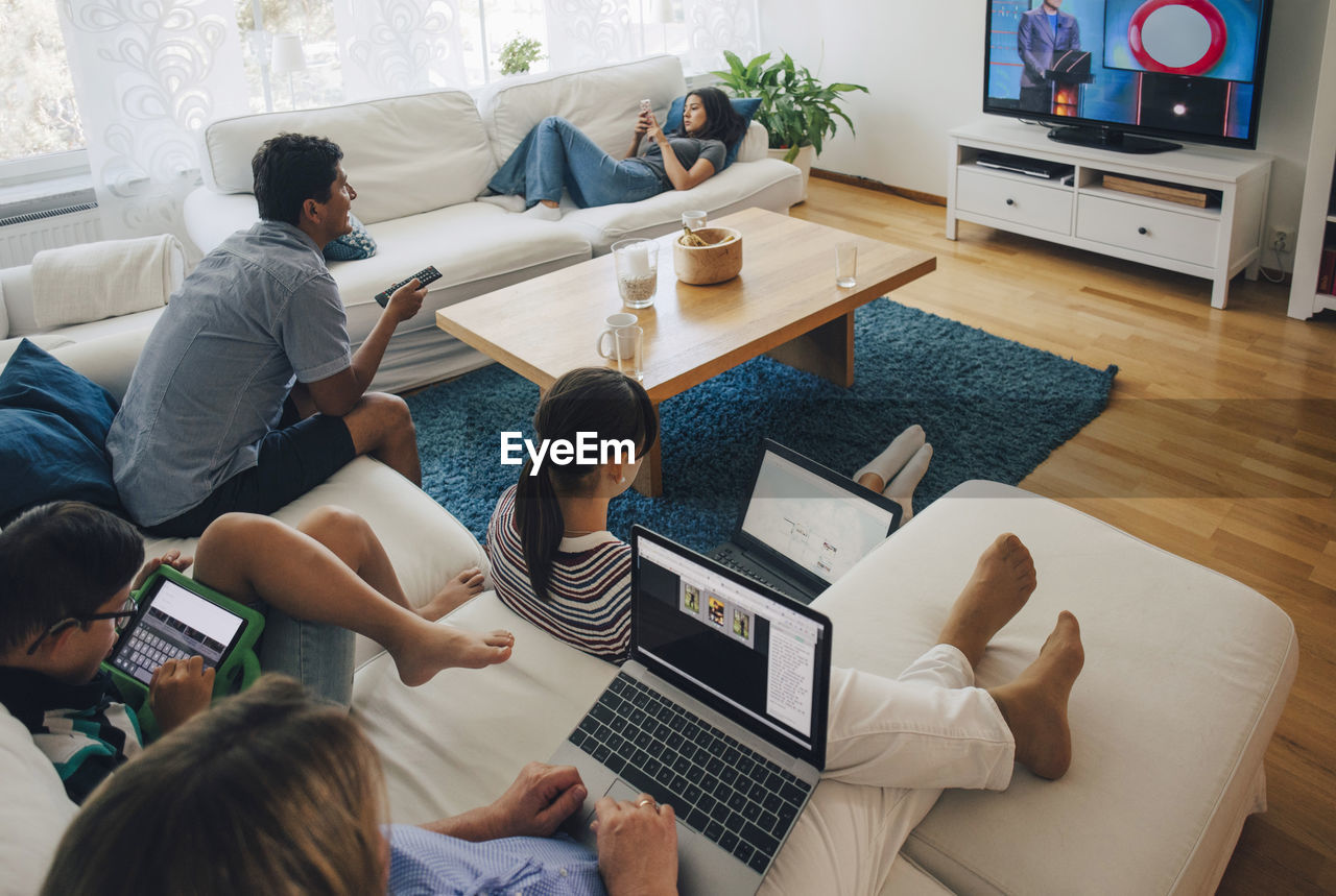 High angle view of family using technologies while relaxing in living room at home