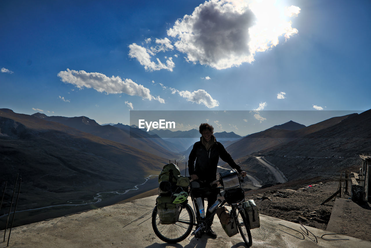 Man standing with bicycle against mountain and sky